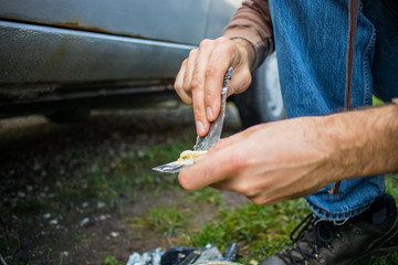 Detail of an amateur mechanic applying polyester putty to repair the sill of his beat up rusty car. Fixing underside of a car with putty.