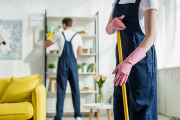 selective focus of woman and man in overalls cleaning modern living room