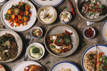 From above of various eastern dishes and snacks arranged with sauces and cutlery on gray surface