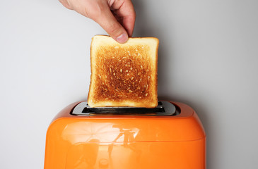 hand toast and orange toaster on a light background - obrazy, fototapety, plakaty