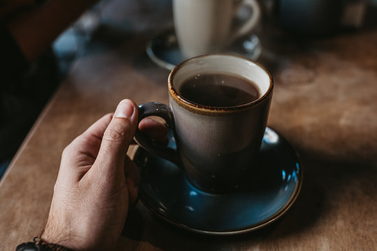 Crop hands of unrecognizable female sitting at wooden table holding hot coffee in a rustic mug - Powered by Adobe