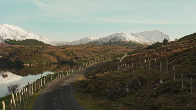 Picturesque scenery of asphalt road with fence near river and mountain ranges in Ireland