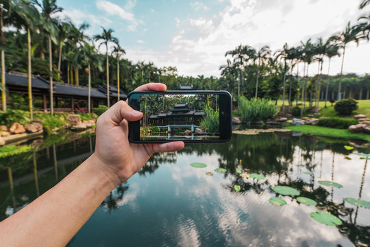 Crop hand using smartphone and taking photo of oriental building on tropical lake of Qingxiu Mountain, China