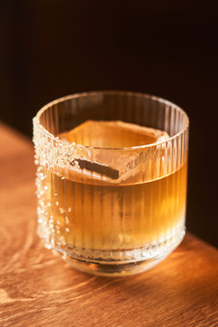 Short glass of amber alcohol whiskey cocktail with ice decorated with sugar placed on wooden counter with black background