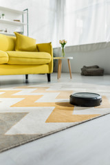 selective focus of modern robotic vacuum cleaner washing carpet near sofa in living room