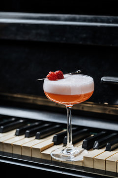 Red alcohol cocktail in stylish glass with white foam decorated with fresh raspberry on piano keys in restaurant