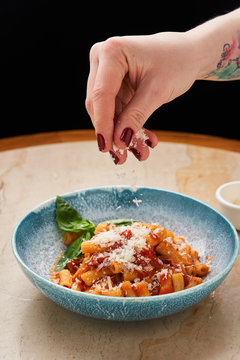 Crop female hand sprinkling with grated cheese on noodles with tomato sauce and basil leaves in blue bowl 