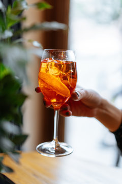 Anonymous woman holding alcohol cocktail with aperol and campari decorated with slices of orange in restaurant 