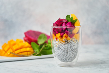 Chia pudding decorated with slices of mango red pitaya and fresh mint in glass with fresh ingredients on blurred background