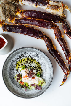 Top view of crab core with cucumbers and basil placed on plate near jug with tomato sauce and boiled king crab legs on white background