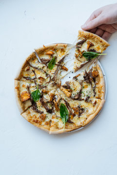 Overhead anonymous person taking slice of palatable seafood pizza with mushrooms and basil against white background
