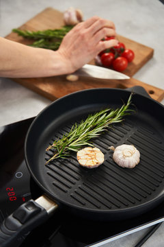 Grill pan with rosemary and garlic next to cooking woman