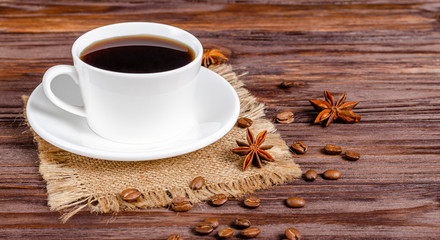Cup of black aromatic coffee in a white cup with anise stars and cinnamon sticks on a wooden background.