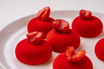 Closeup delectable cookies with vivid red icing and raspberries on top placed on white plate