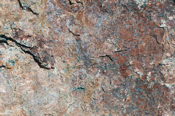 Closeup of a big solid stone in red, orange and black tones. In this photo you can see the rustic texture of the uneven surface of the rock in detail. Perfect grungy background image. Color photo.