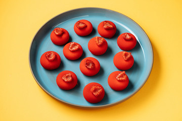 From above red ball shaped cookies with fresh raspberries placed on plate on yellow background