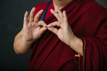 Closeup of hands of crop praying Tibetan monk in traditional red robe with mudra symbolic hands gesture
