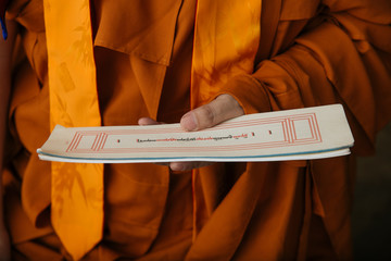 Crop Tibetan Buddhist monk in orange clothes holding paper with holy ritual text