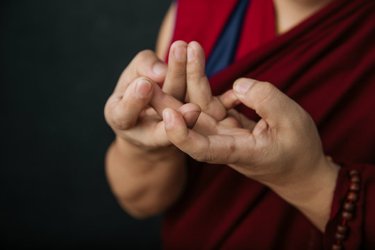 Closeup of hands of crop praying Tibetan monk in traditional red robe with mudra symbolic hands gesture