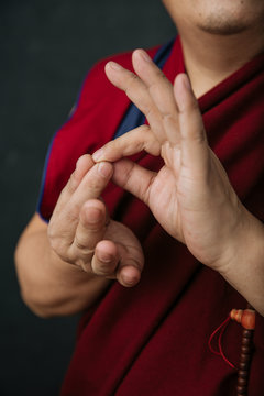 Closeup of hands of crop praying Tibetan monk in traditional red robe with mudra symbolic hands gesture