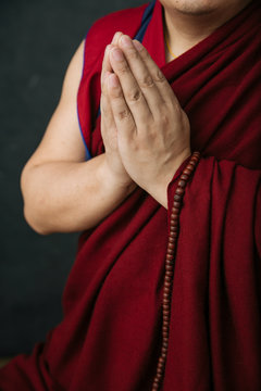 Crop Tibetan monk in traditional red robe with prayer beads and hands folded in Namaste mudra