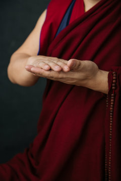 Closeup of hands of crop praying Tibetan monk in traditional red robe with mudra symbolic hands gesture