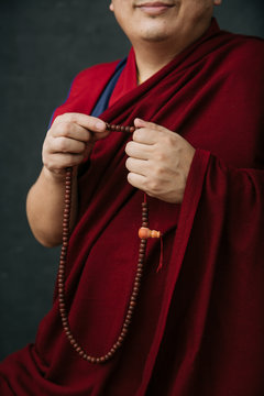 Side view of crop Buddhist monk in traditional red clothes holding prayer beads in hand