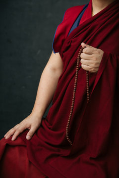 Side view of crop Buddhist monk in traditional red clothes holding prayer beads in hand