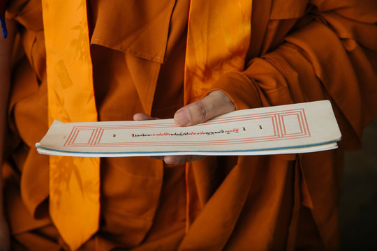 Crop Tibetan Buddhist monk in orange clothes holding paper with holy ritual text