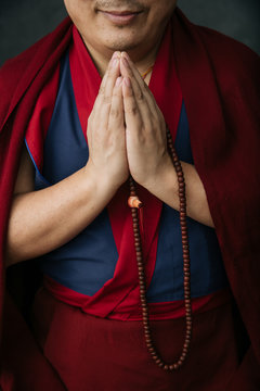 Side view of crop Buddhist monk in traditional red clothes holding prayer beads in hand