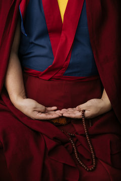 Side view of crop Buddhist monk in traditional red clothes holding prayer beads in hand