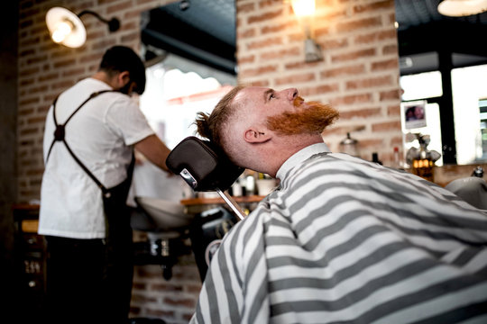 Redhead man sitting in barbershop waiting for anonymous barber on the background