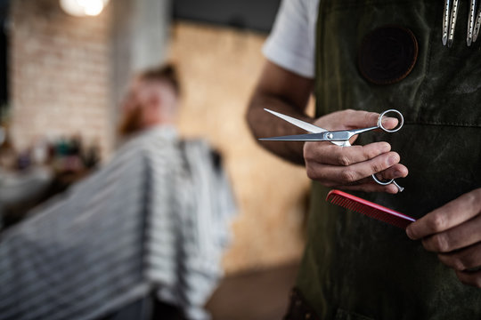 Unrecognizable crop man hairdresser holding scissors and comb in modern barbershop