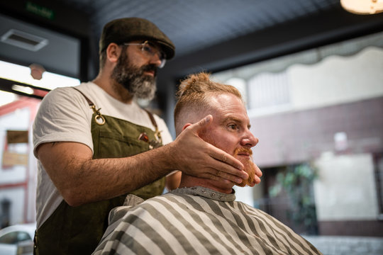 Barber doing face massage to handsome redhead man with sitting in chair