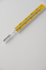 Top view of yellow mercury thermometer, diagonally, on white background with copy space