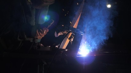 Industrial worker in a protective mask using modern welding machine for welding metal structures in industrial production at a metal processing plant. bright light and sparks from welding.