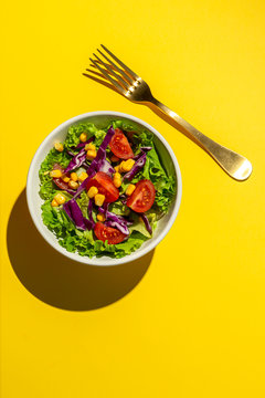 Fresh lettuce salad with Cherries tomatoes, red onion and corn, sunlight on pink background from above. Healthy food. Vegan food.