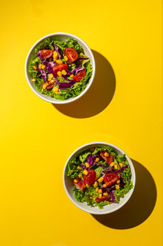 Fresh lettuce salad with Cherries tomatoes, red onion and corn, sunlight on pink background from above. Healthy food. Vegan food.