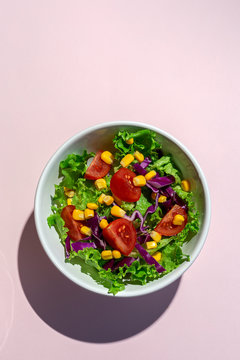 Fresh lettuce salad with Cherries tomatoes, red onion and corn, sunlight on pink background from above. Healthy food. Vegan food.