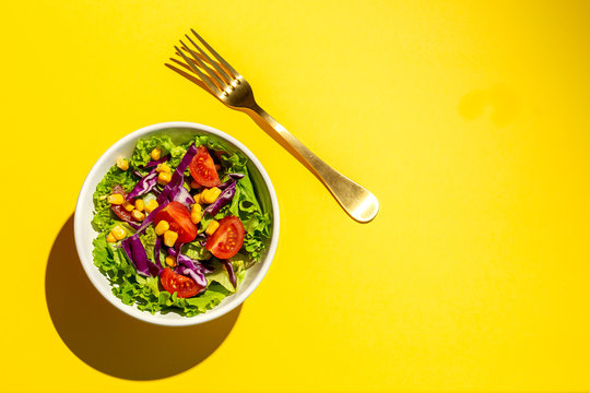 Fresh lettuce salad with Cherries tomatoes, red onion and corn, sunlight on pink background from above. Healthy food. Vegan food.