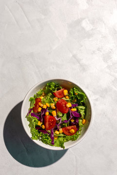 Fresh lettuce salad with Cherries tomatoes, red onion and corn, sunlight on pink background from above. Healthy food. Vegan food.