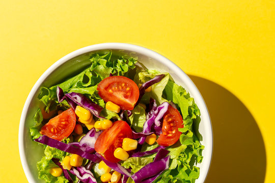 Fresh lettuce salad with Cherries tomatoes, red onion and corn, sunlight on pink background from above. Healthy food. Vegan food.