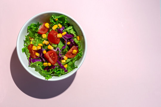 Fresh lettuce salad with Cherries tomatoes, red onion and corn, sunlight on pink background from above. Healthy food. Vegan food.