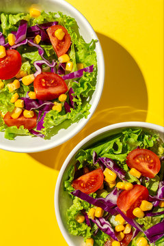 Fresh lettuce salad with Cherries tomatoes, red onion and corn, sunlight on pink background from above. Healthy food. Vegan food.