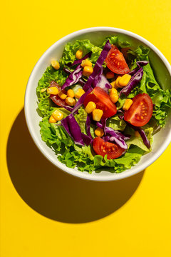Fresh lettuce salad with Cherries tomatoes, red onion and corn, sunlight on pink background from above. Healthy food. Vegan food.