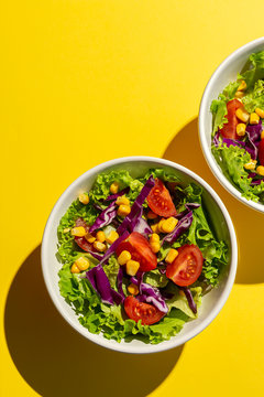 Fresh lettuce salad with Cherries tomatoes, red onion and corn, sunlight on pink background from above. Healthy food. Vegan food.