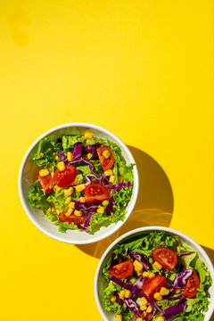Fresh lettuce salad with Cherries tomatoes, red onion and corn, sunlight on pink background from above. Healthy food. Vegan food.