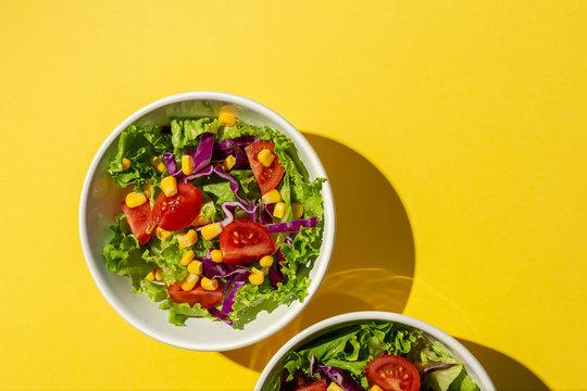 Fresh lettuce salad with Cherries tomatoes, red onion and corn, sunlight on pink background from above. Healthy food. Vegan food.
