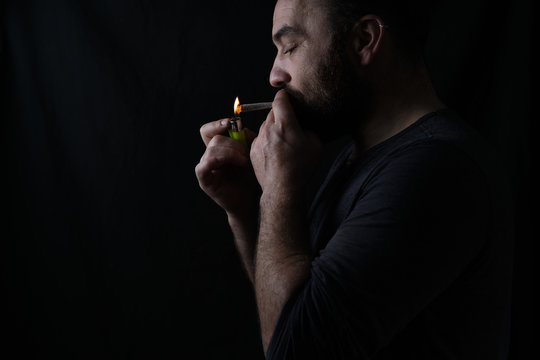 Side view of crop concentrated male smoker lighting up marijuana blunt on black background