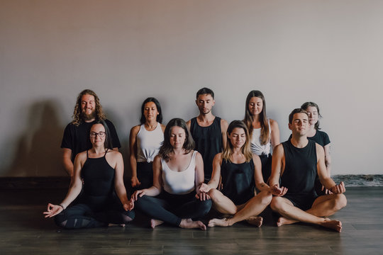 High angle of group of young serene women and men in sportswear with eyes closed and Gyan Mudra relaxing and meditating while sitting in padmasana position against white wall in contemporary yoga studio